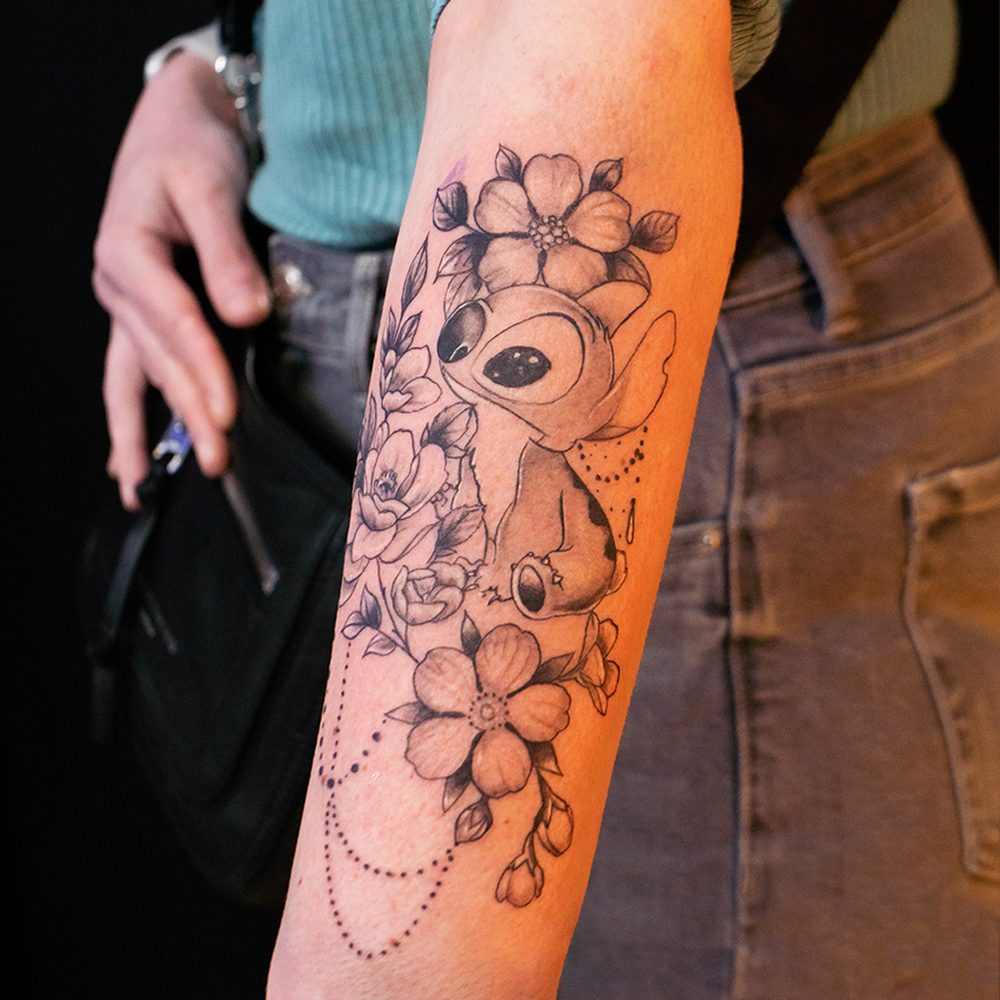 Fineline Blumen-Tattoo mit Stitch-Motiv am Unterarm